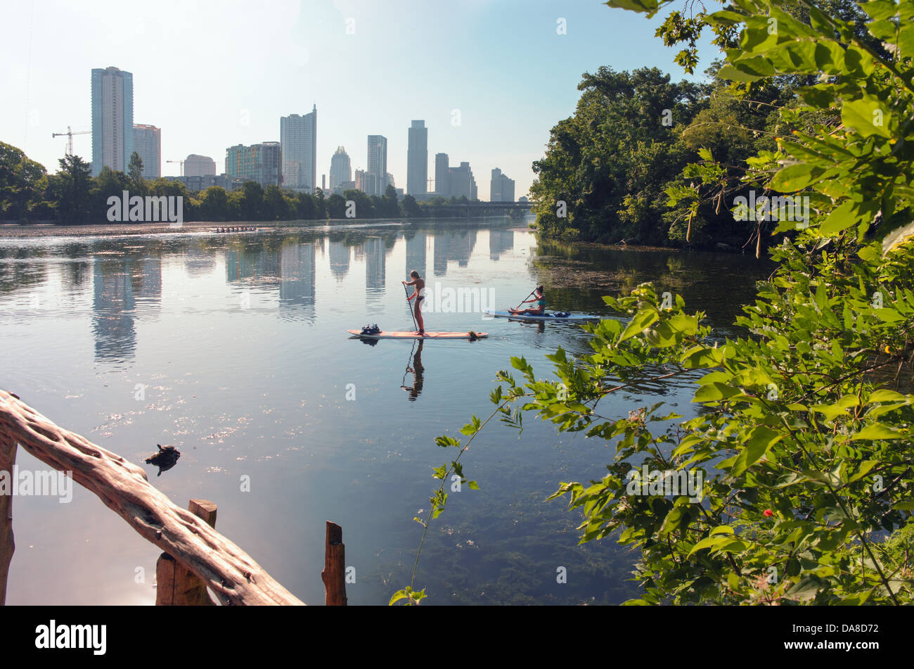 Two young females maneuver their paddle boards on Ladybird Lake in Austin, Texas. Downtown Austin is visible in the background. Stock Photo