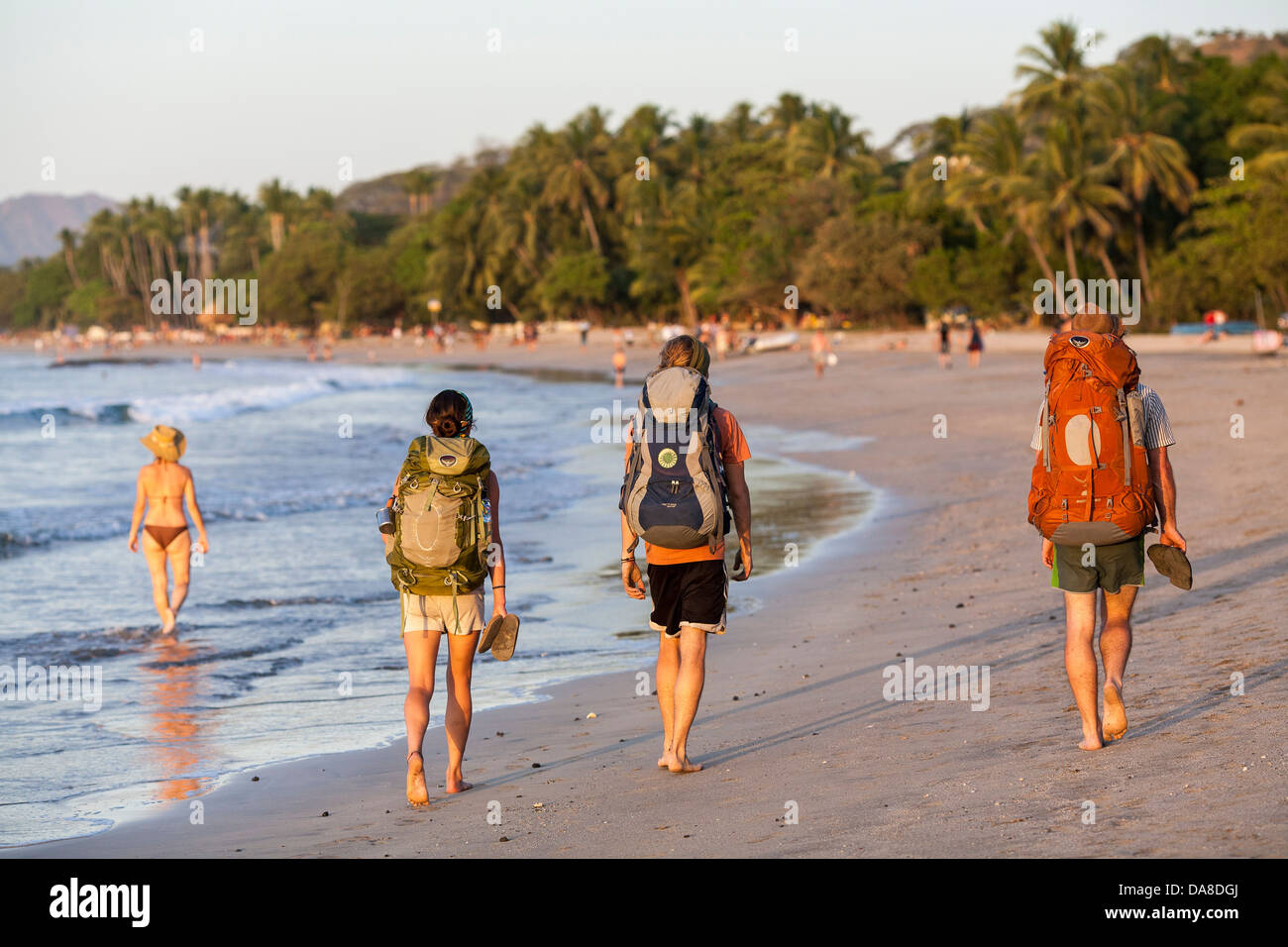 Backpackers walk along the beach wearing a rucsac in Playa Tamarindo Guanacaste Costa Rica Stock Photo