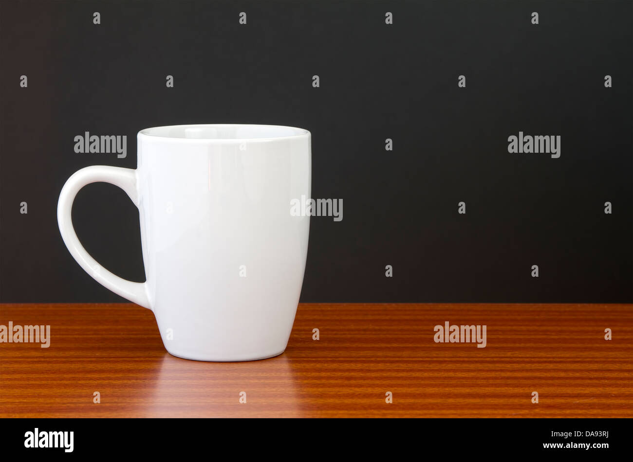 White mug on dark wooden table with black wall Stock Photo