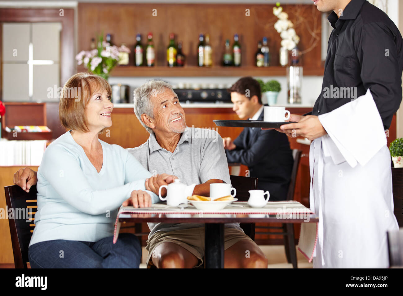 Waiter serving two seniors in a coffee shop for breakfast Stock Photo