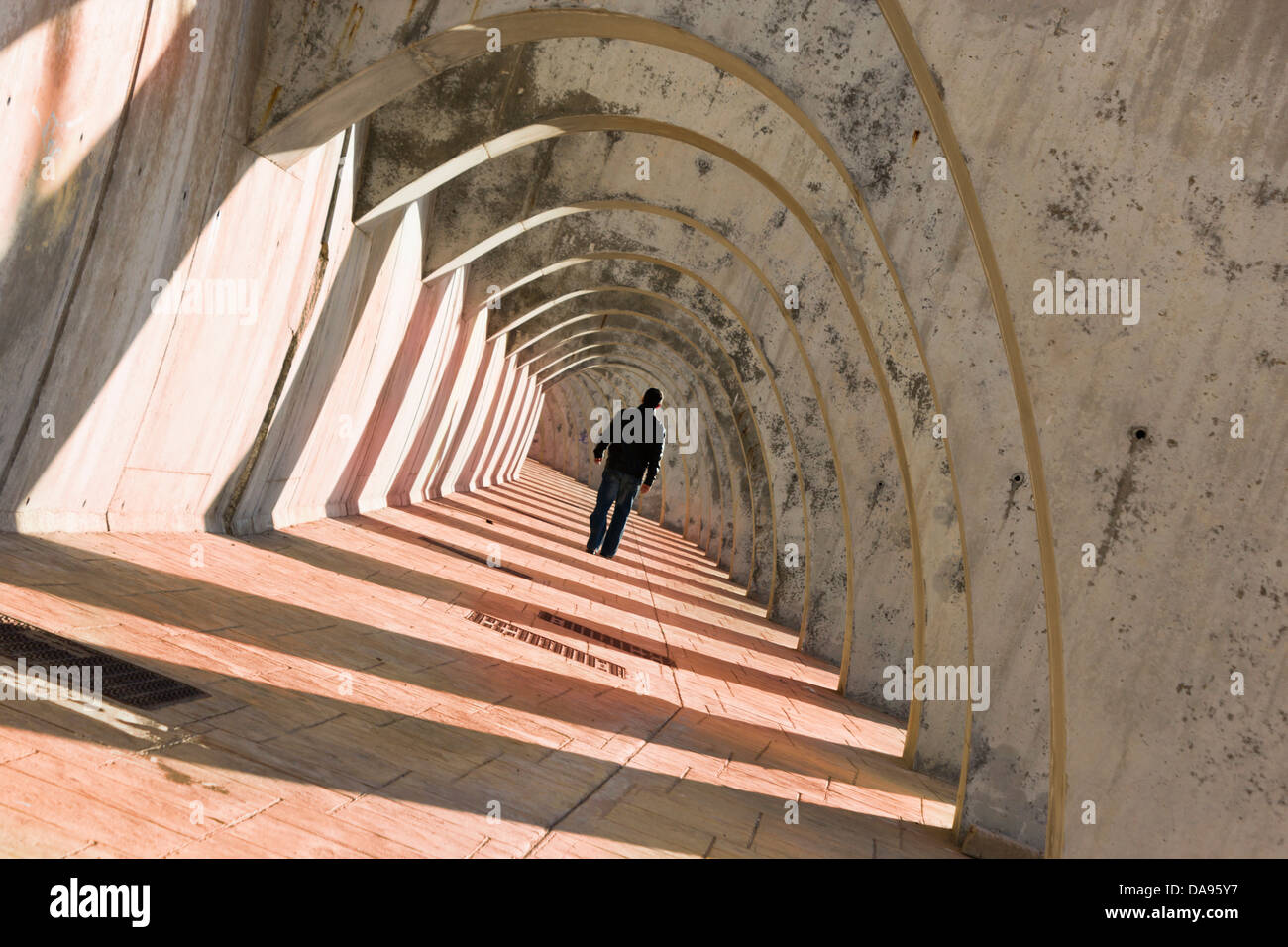 Mysterious man walking under arched walkway. Stock Photo