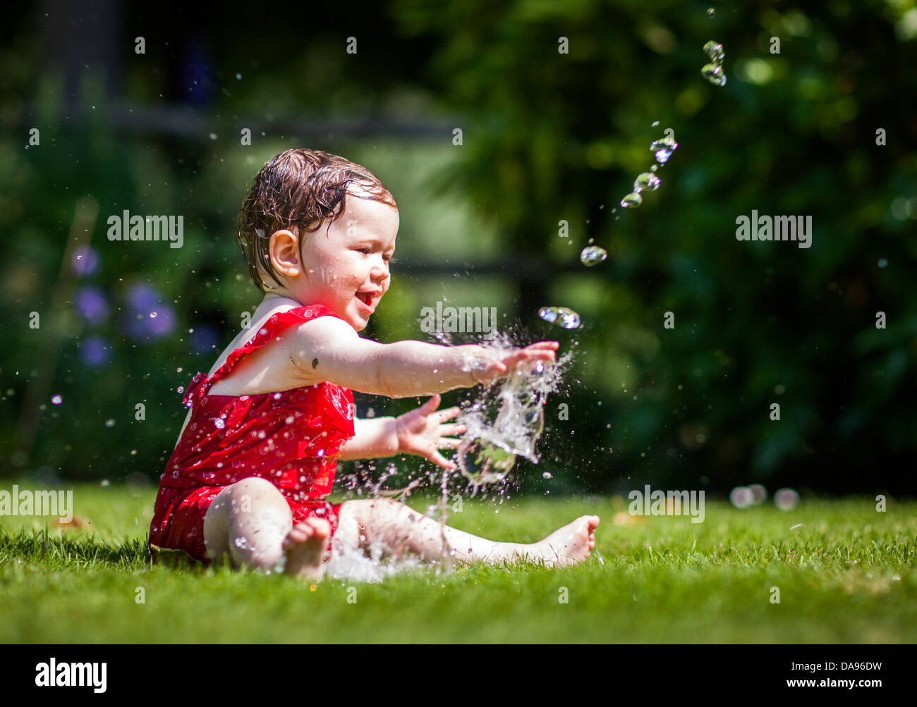 A baby squeals in delight as she cools down with water from a hose Stock  Photo - Alamy