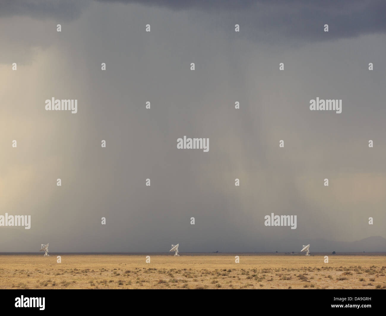 Rain falls in the distance on three large radio satellites on the Plains of San Agustin at the Very Large Array Observatory, NM Stock Photo