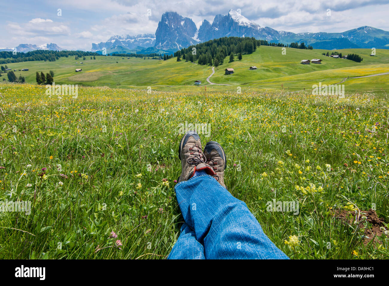 Crossed legs of a hiker at Alpe di Siusi or Seiser Alm with Sassolungo mountain behind, Dolomites, Alto Adige South Tyrol, Italy Stock Photo
