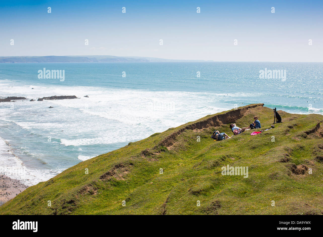 Three people and their dog relax in the sun above Sandymouth Bay, north Devon, England, on a sunny summer's day. Stock Photo
