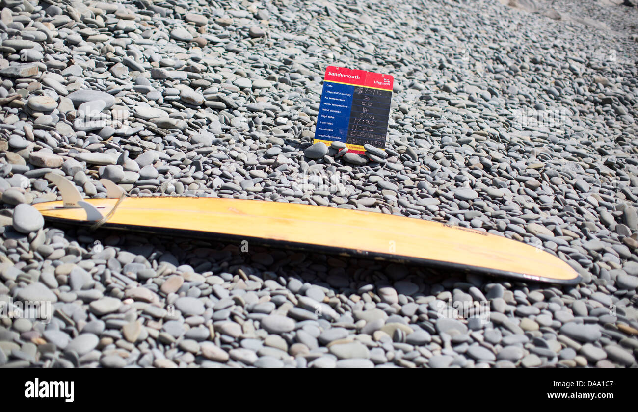 Yellow surfboard and lifeguard information sign on a pebble beach in Sandymouth Bay, north Devon, England. Stock Photo