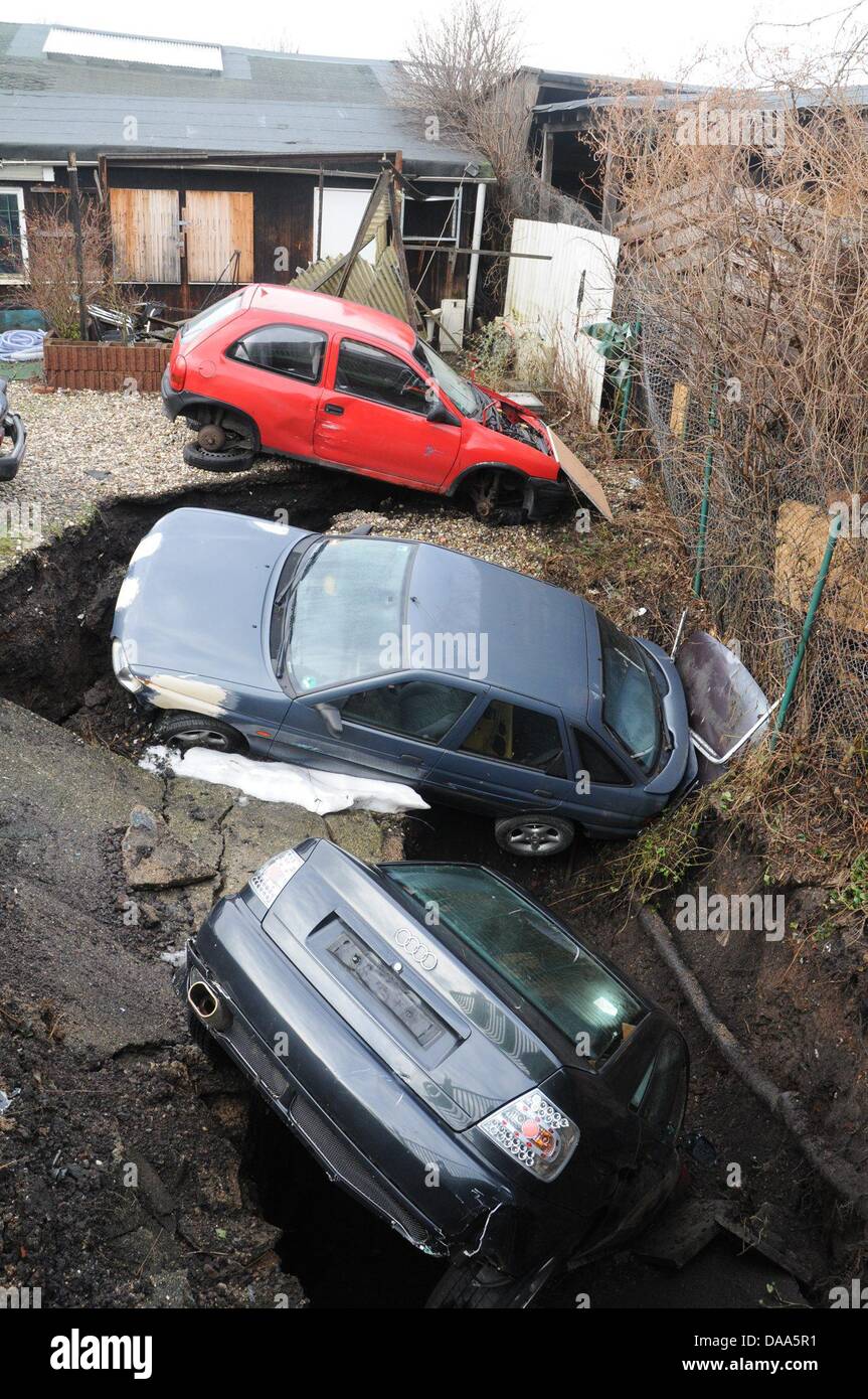 Three cars lie in a hole on an auto repair shop's lot in Essen, Germany, 09 January 2011. The auto repair shop lies on an old colliery area, according to police statements, however it is unclear whether the eight meter deep, nine meter wide hole was caused by mining activites or meltwaters. Photo: KDF-TV/STEPHAN WITTE Stock Photo