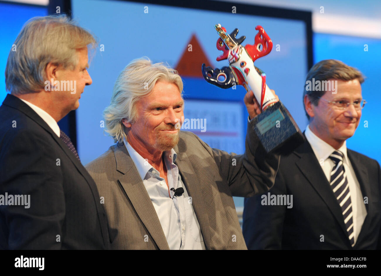 British enterpriser and billionaire Richard Branson is awarded with the German Media Prize 2010 at the Congress Center of Baden Baden, Germany, 24 January 2011. Despite his cruciate ligament rupture, he showed up on crutches to receive his prize. To his left stands media entrepreneur Karlheinz Koegel who founded the prize, to his right German Foreign Minister Guido Westerwelle, who Stock Photo