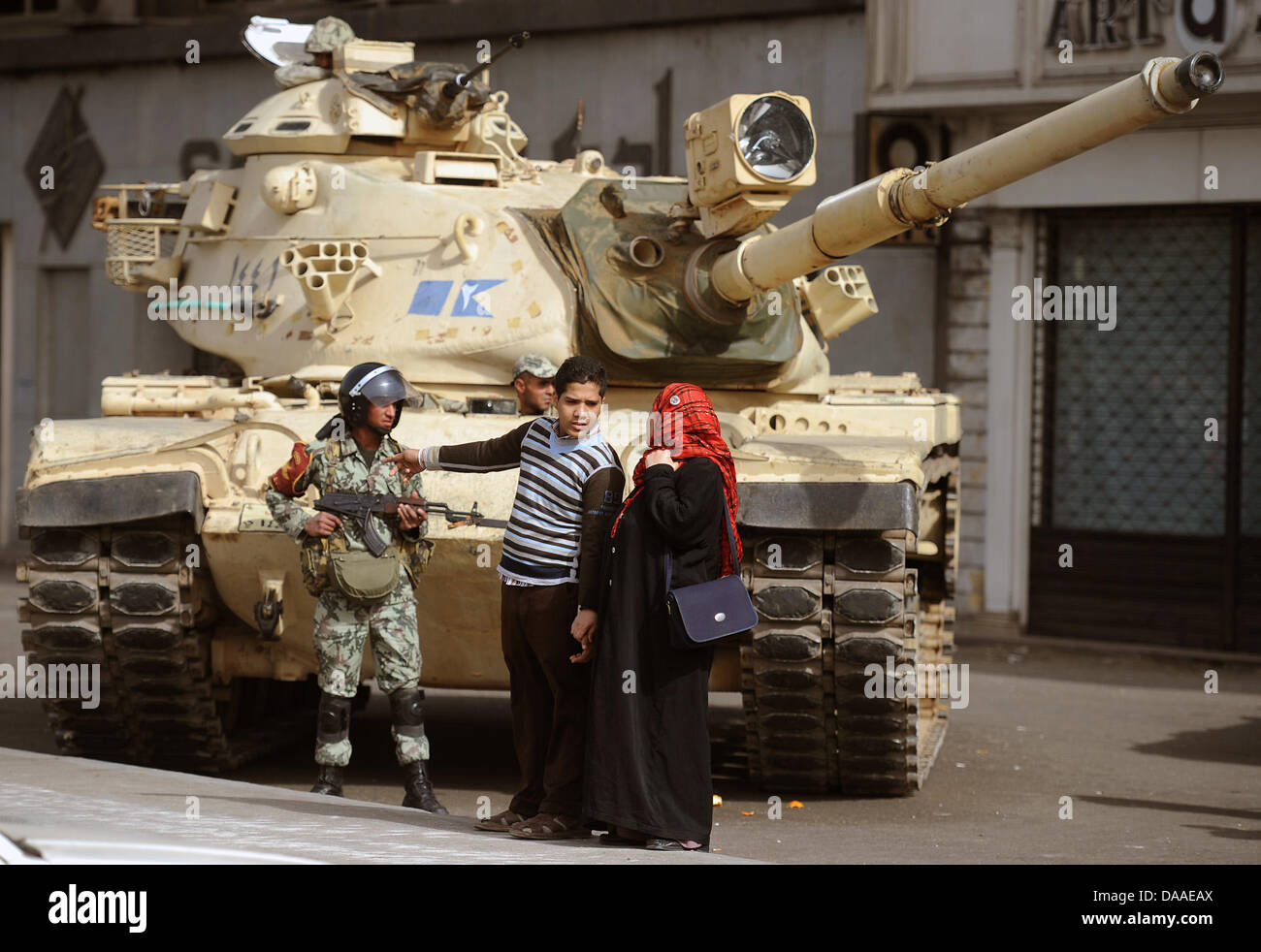 Ein junger Mann und eine Frau mit Kopftuch reden am Samstag (29.01.2011) vor einem Panzer mit einem Soldaten, der aber sein Gewehr weiter im Anschlag behält, in der Innenstadt von Kairo. Die Plünderungen und Ausschreitungen in der ägyptischen Hauptstadt Kairo sind auch am Samstagmorgen weitergegangen. Dies berichteten Augenzeugen. In zwei Kairoer Vierteln seien aus gestürmten Poliz Stock Photo