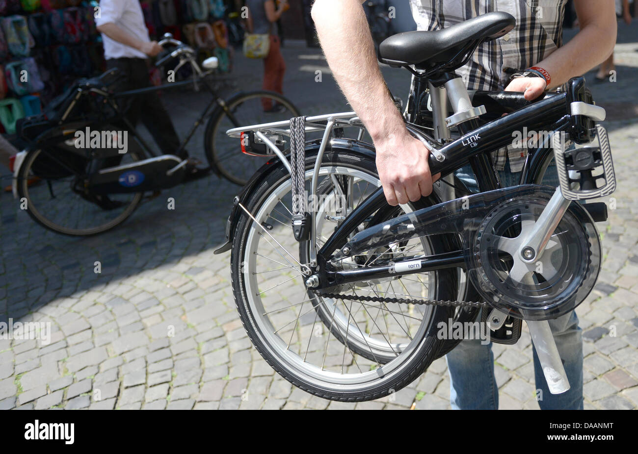 Employee Vincent Becker carries a foldable bicycle from the municipal works in Muenster, Germany, 09 July 2013. The Muenster municipal works are renting foldable bicycles to their customers to connect all forms of public transportation from door to door. The bicycle can be used to cycle from home to the bus stop and then folded and take on the bus. Photo: CAROLINE SEIDEL Stock Photo