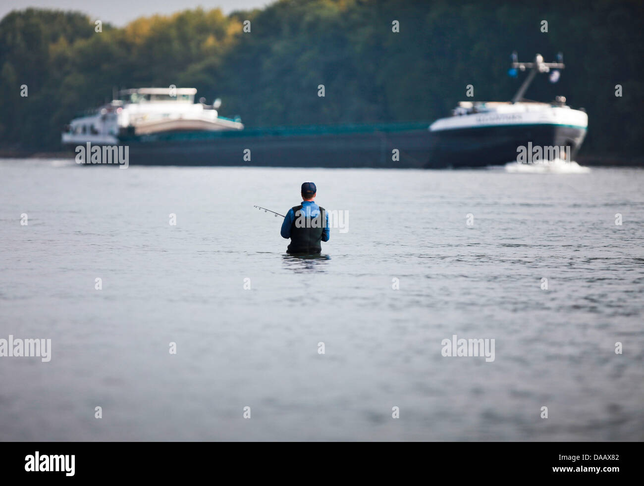 A fisherman stands up to his hips in the River Rhine as a river barge passes by near Nierstein, Germany, 20 September 2011. Photo: Frank Rumpenhorst Stock Photo