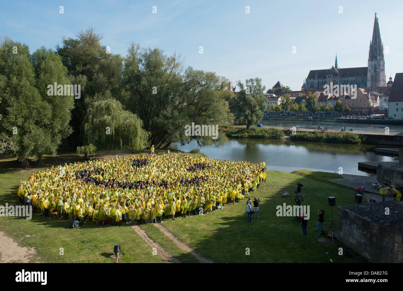 Numerous people stand wearing yellow and black raincaps on the Jahn Island and form a smiley in Regensburg, Germany, 24 September 2011. Organizers wanted to break the record for the largest smiley made of people with the action 'Regensburg smiles' with almost 3000 participants. Unfortunately, only around half of the participants came. Photo: ARMIN WEIGEL Stock Photo