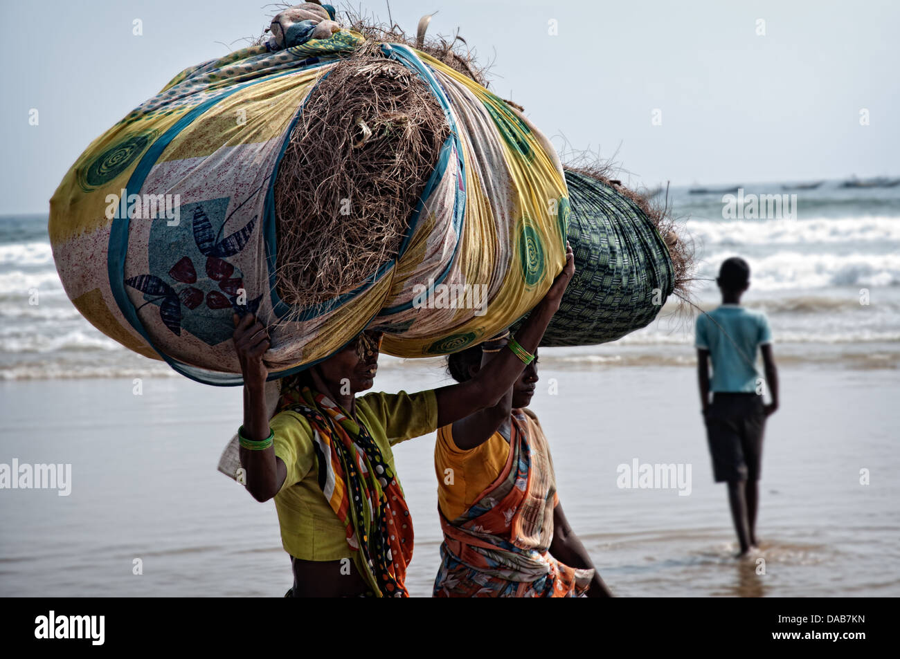 Women carrying huge package of leafs on her head through the beach. Puri, Orissa, India Stock Photo