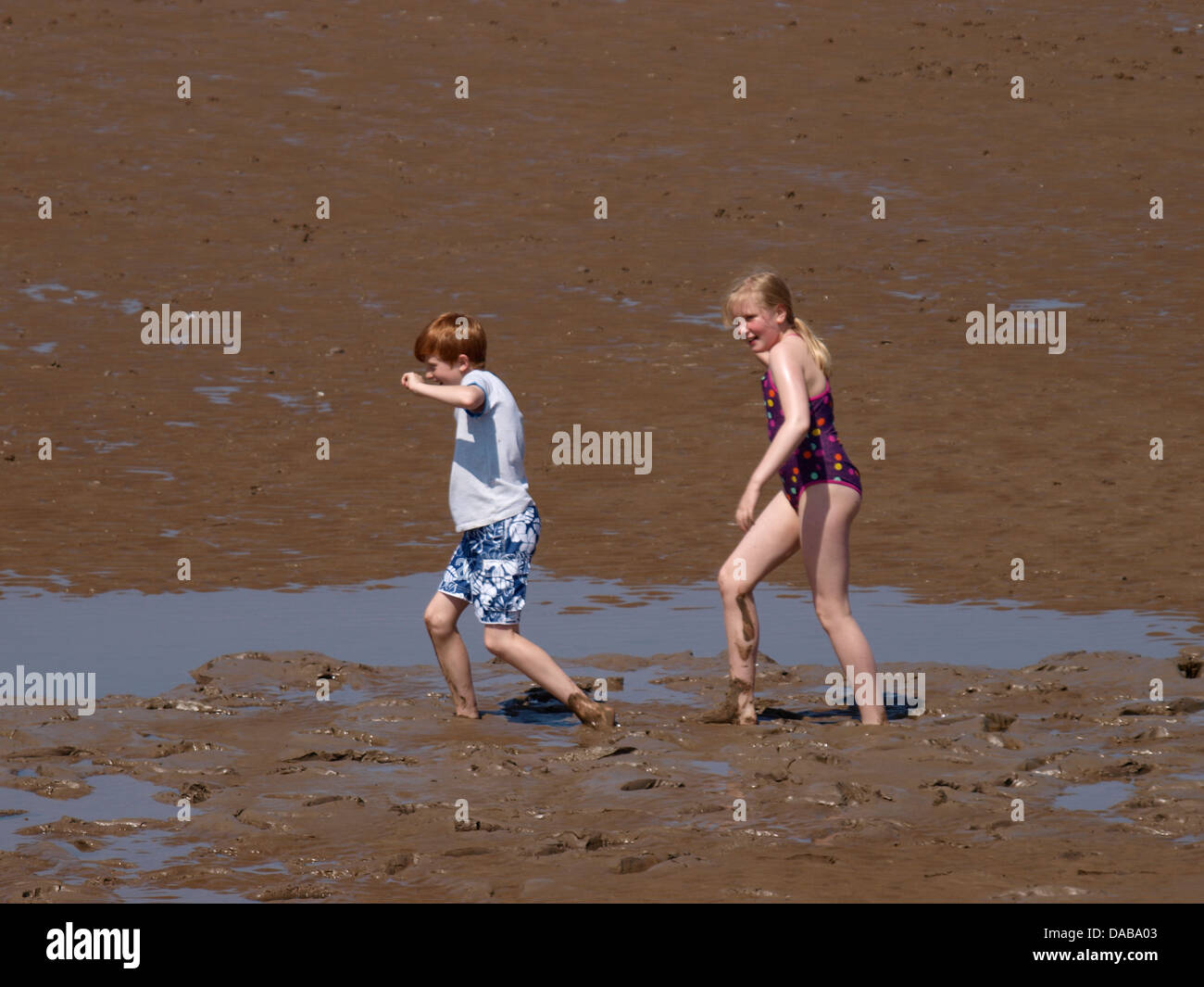 Two kids struggling to walk through the mud of Burnham on Sea beach, Somerset, UK 2013 Stock Photo
