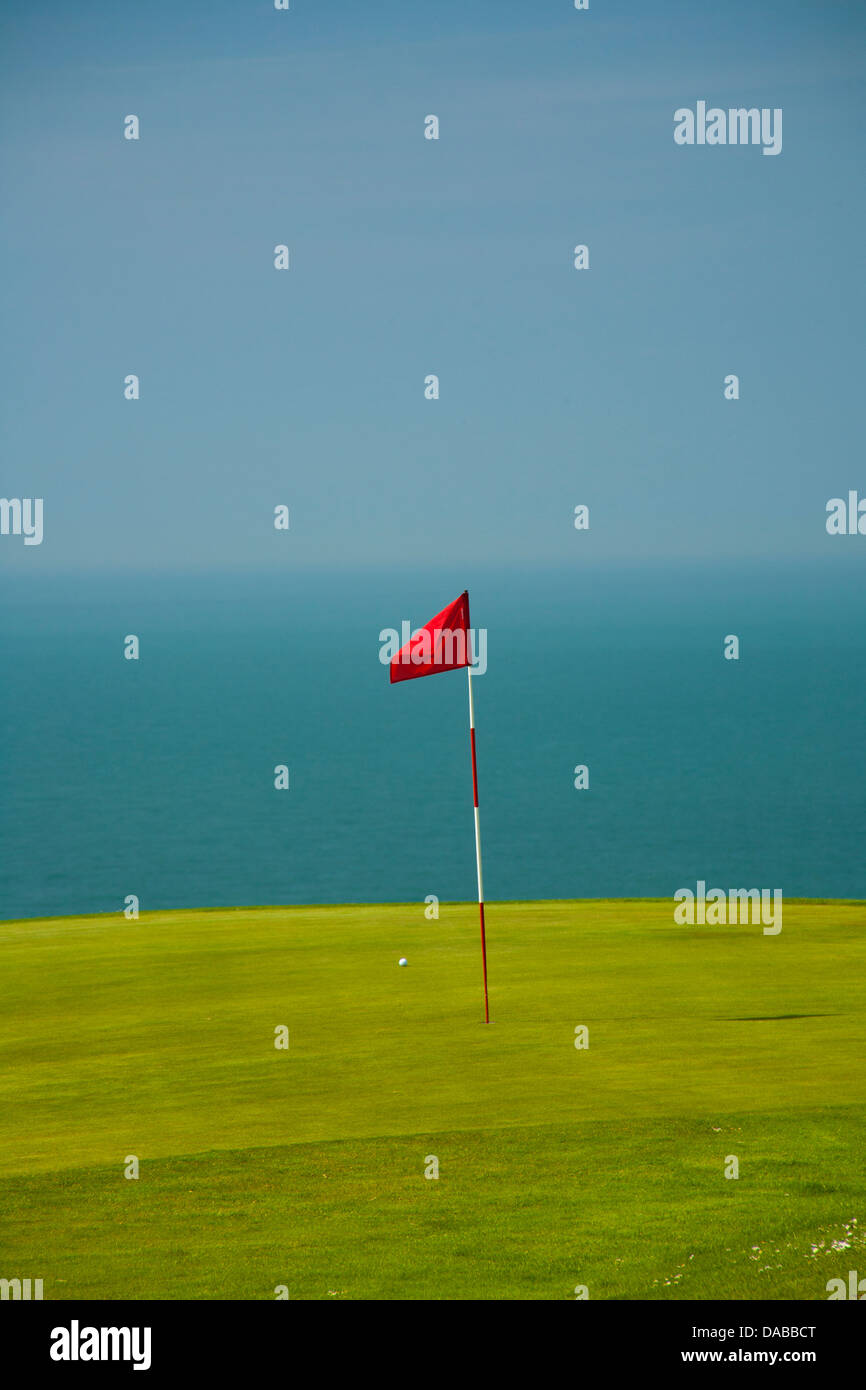 Golf flag in bright green Green with deep blue sea in the background. Stock Photo