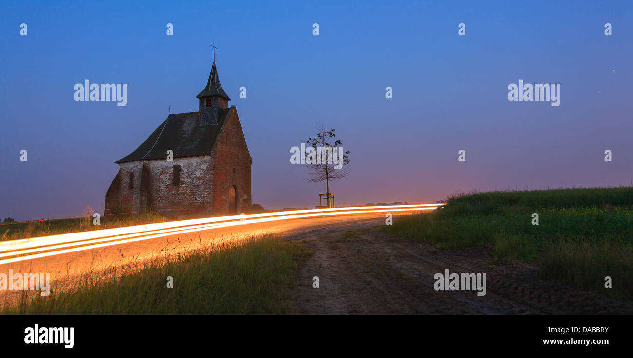 Disturbed quietness of a chapel by a car at dusk with light trails Stock Photo