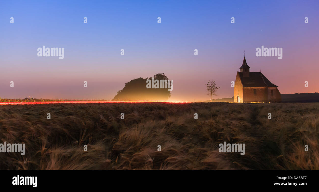 Disturbed quietness of a chapel by a car at dusk with light trails Stock Photo