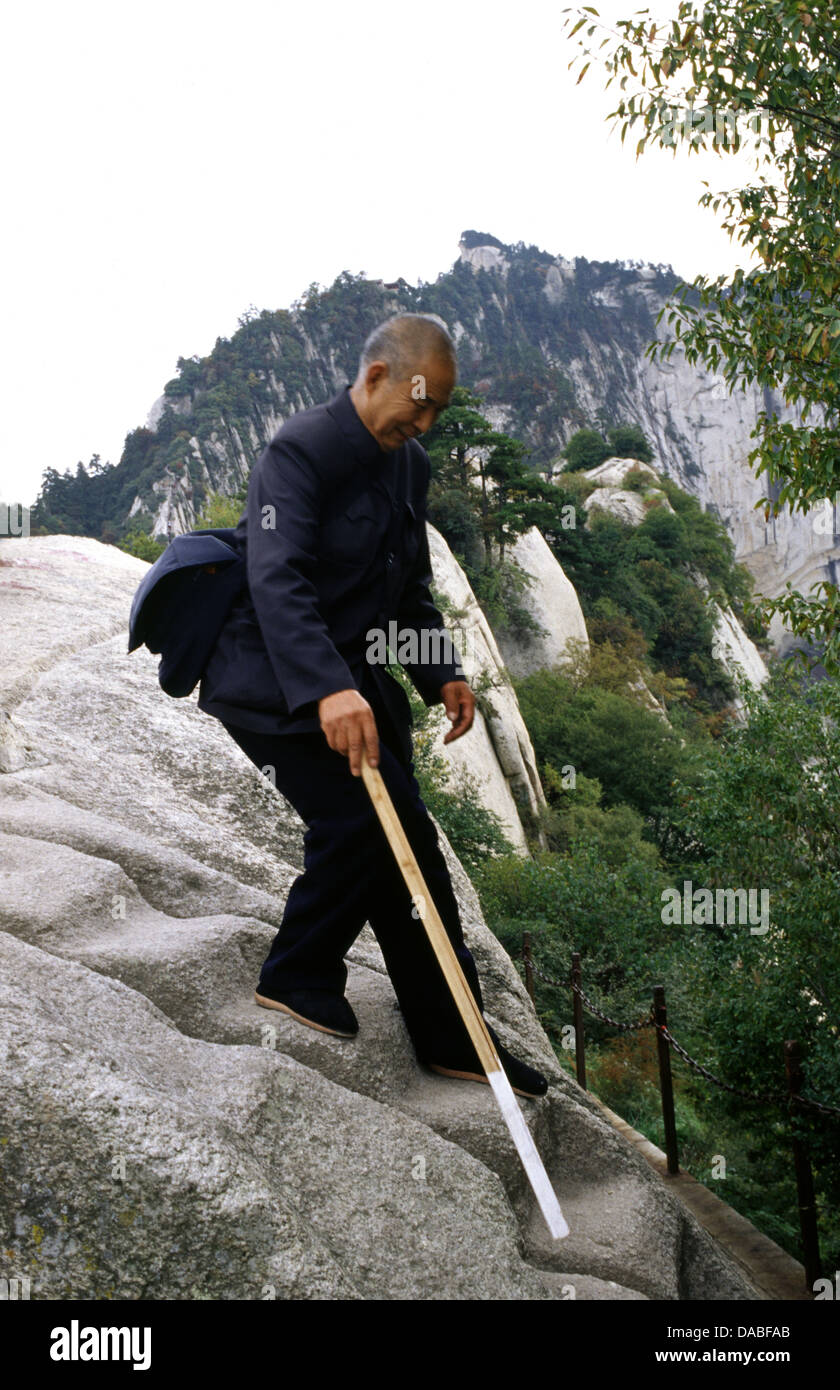 An elderly Chinese man with walking stick descending Hua Shan mountain located near the city of Huayin in Shaanxi province China. Mount Hua is the western mountain of the Five Great Mountains of China, and has a long history of religious significance. Stock Photo