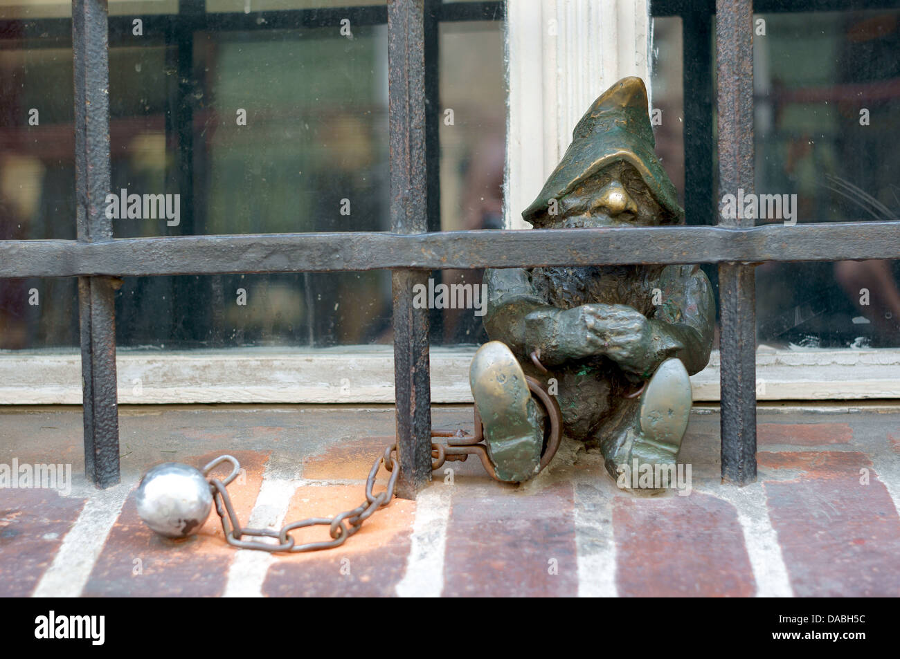 Figurine of dwarf with ball and chain behind iron bars Wroclaw Stock Photo
