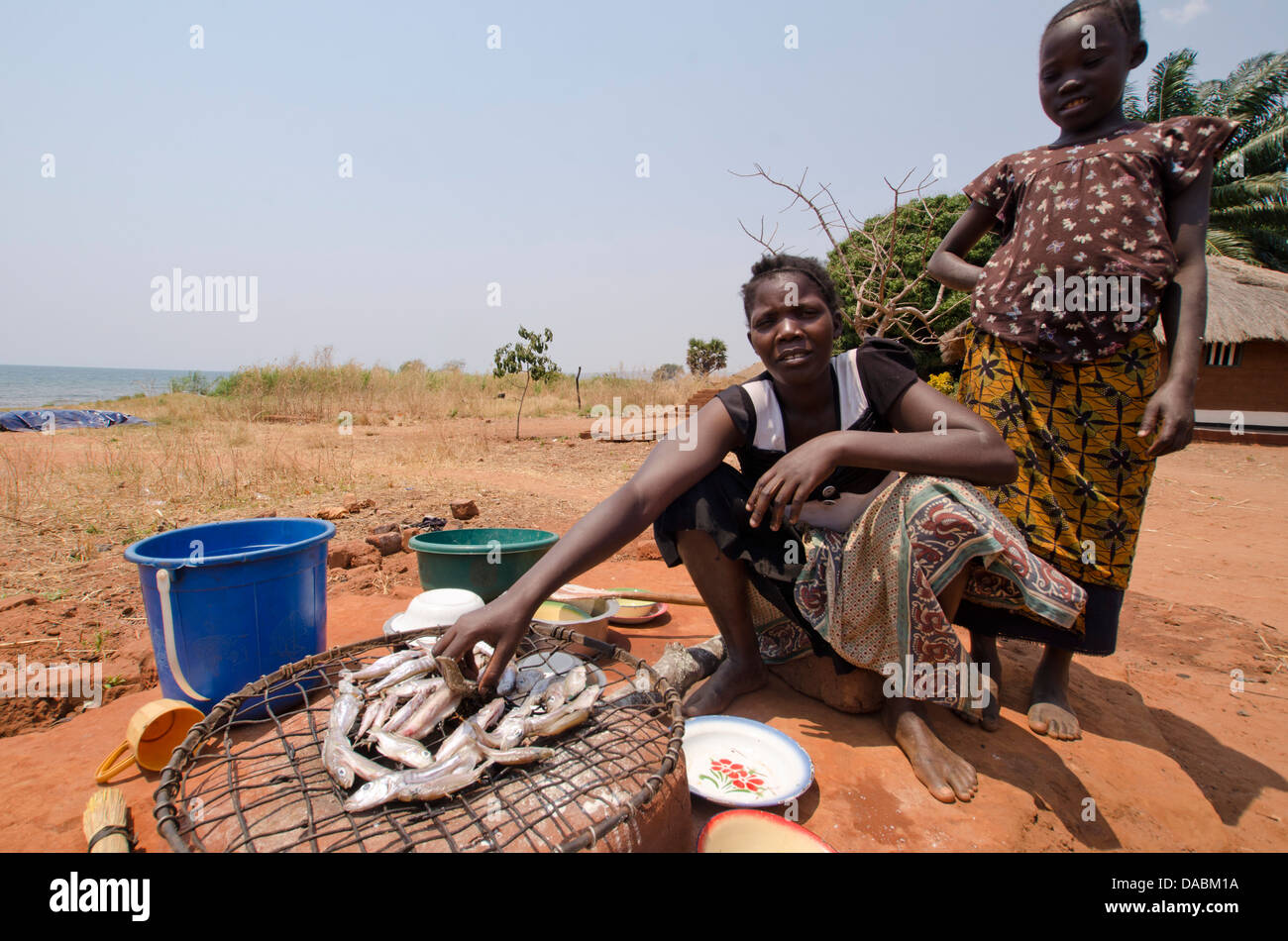 Lady preparing fish for meal with young girl, Talpia, Zambia, Africa Stock Photo