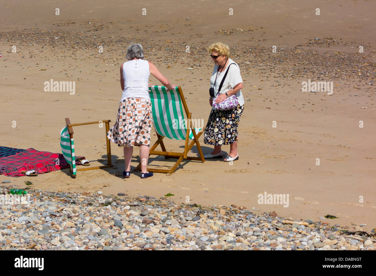 Two ladies on an English beach setting up their hired deck chairs on a hot summer's day Stock Photo