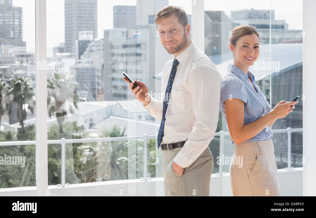 Happy business team standing back to back and texting Stock Photo - Alamy