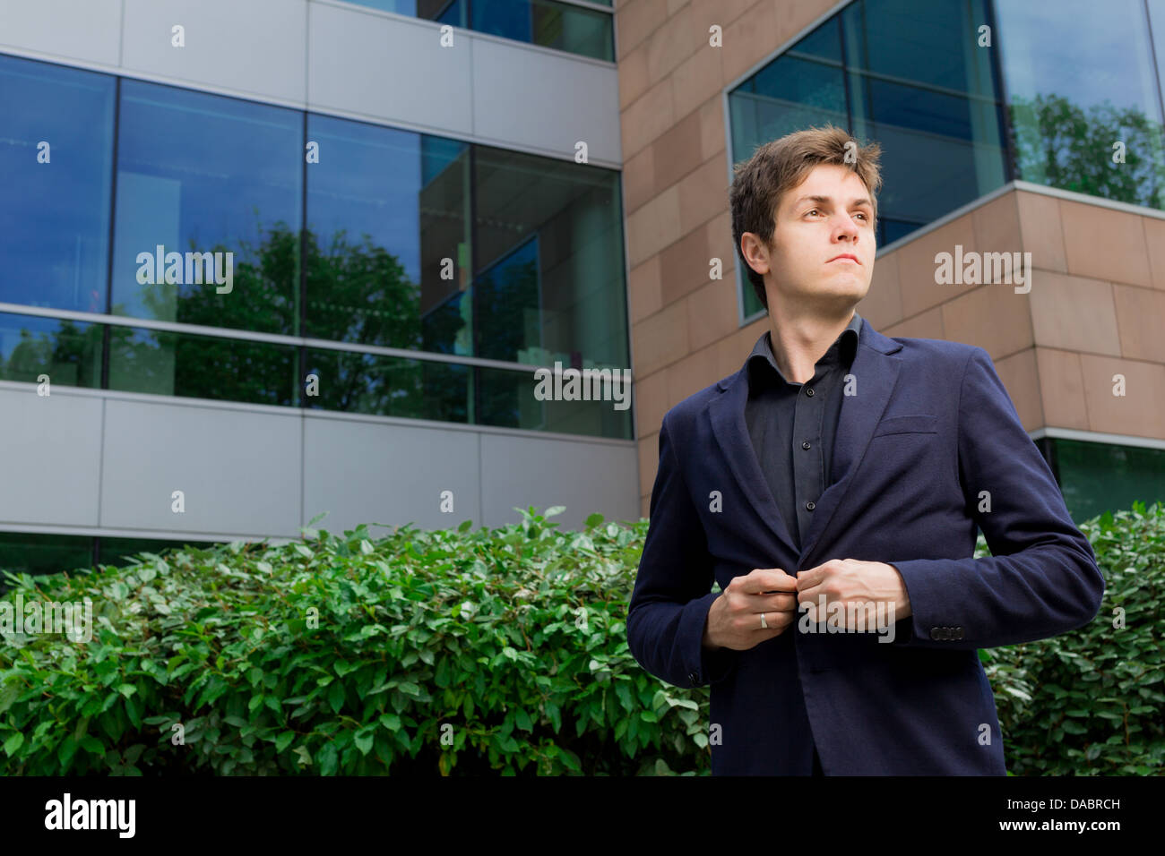 Business man standing in front of office building closing his blazer Stock Photo