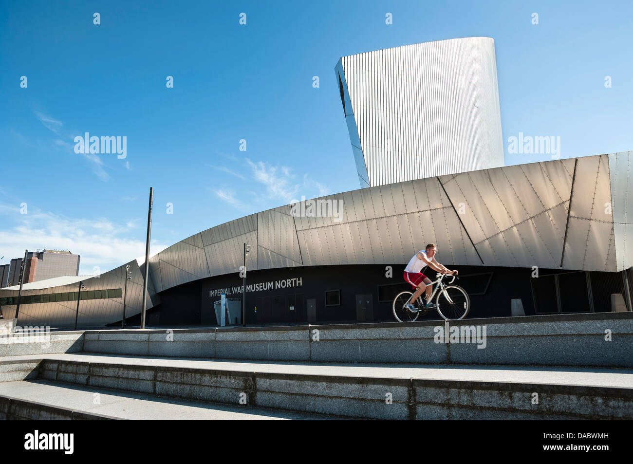 Cyclist riding past the Imperial War Museum North, Manchester, UK Stock Photo