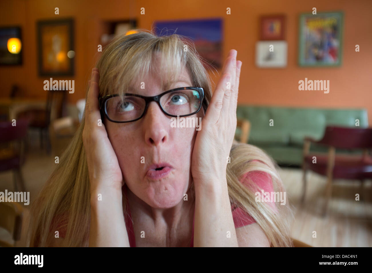 Female wearing glasses pushing her cheeks in with her hands and looking upward. Stock Photo