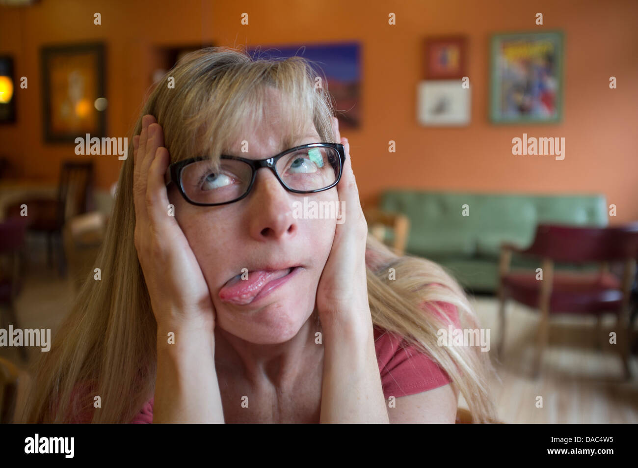 Female wearing glasses pulling cheeks, looking upward and sticking tongue out. Stock Photo