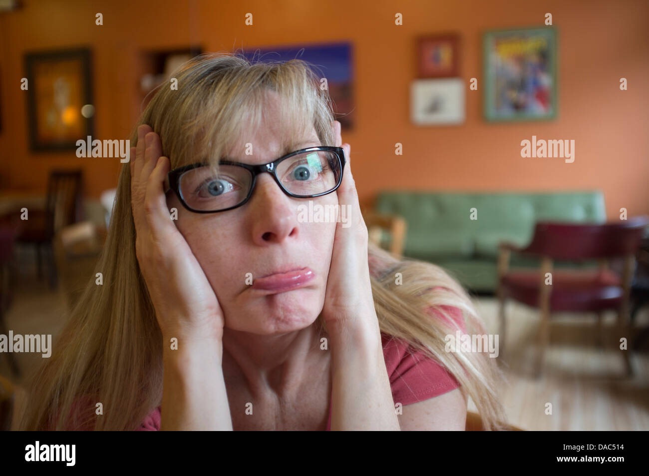Woman with glasses on holding her hands on either side of her face pulling her cheeks back. Stock Photo