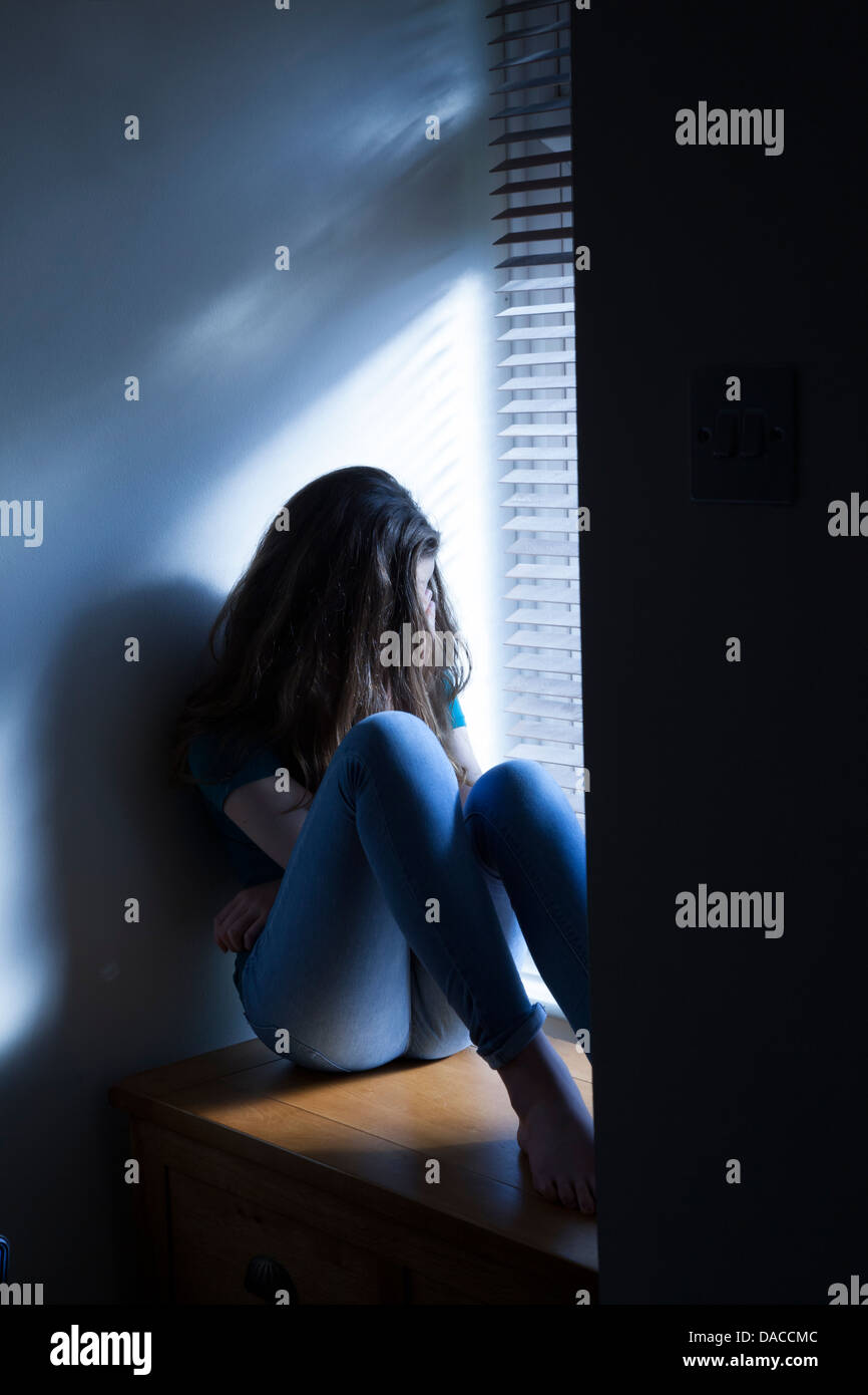 A teenage girl, sitting by a window with light pouring in. Stock Photo