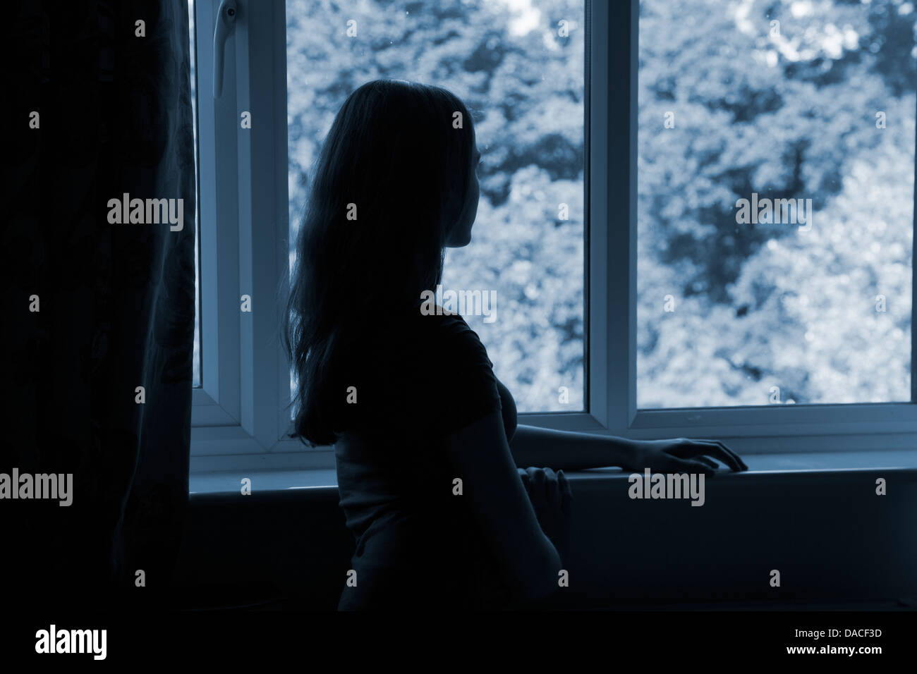 A teenage girl, looking out of a window. Rear/Side view. Stock Photo