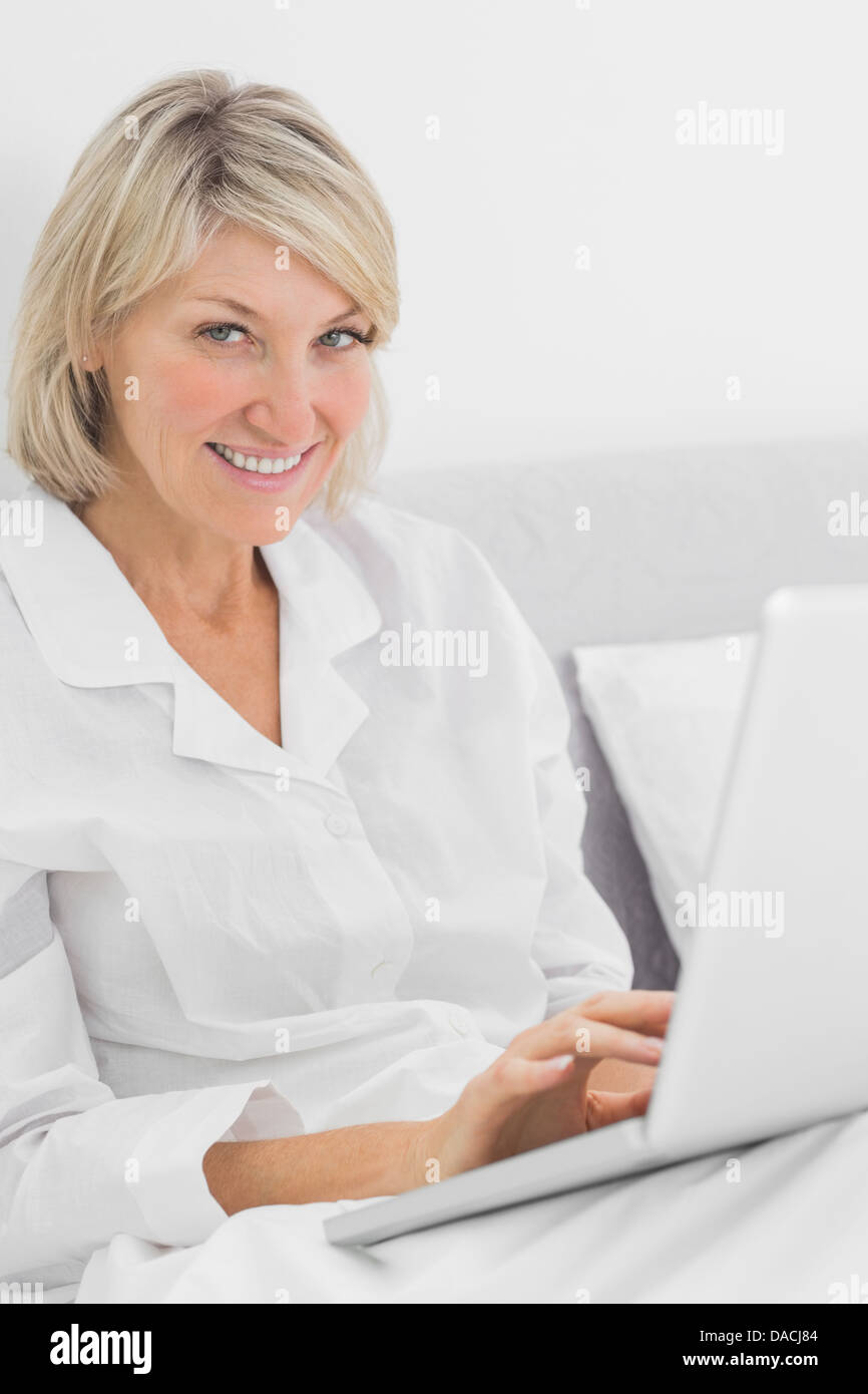 Cheerful woman sitting in bed with laptop looking at camera Stock Photo ...
