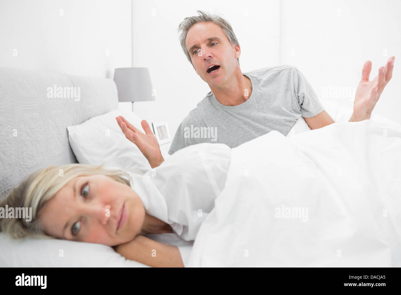 Man pleading with his upset partner in bed Stock Photo