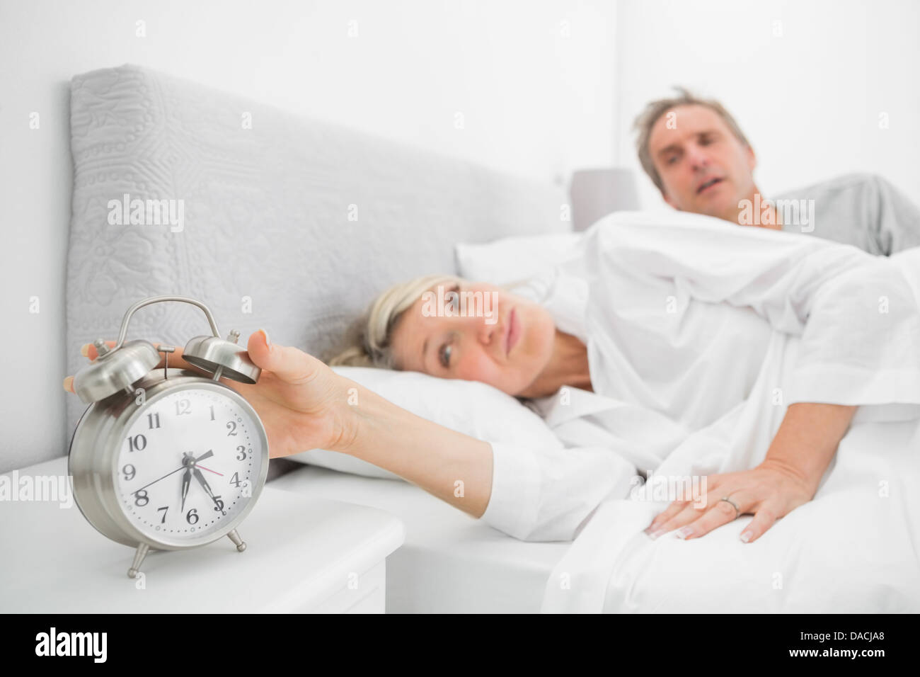 Woman in bed with partner turning off alarm clock Stock Photo