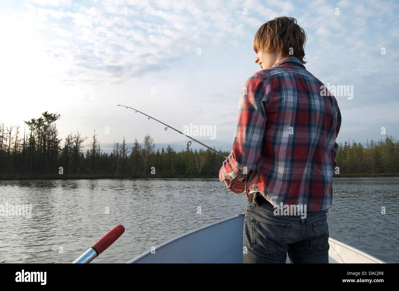 Teen male fishing off of the back of a row boat on a small inland lake. Stock Photo