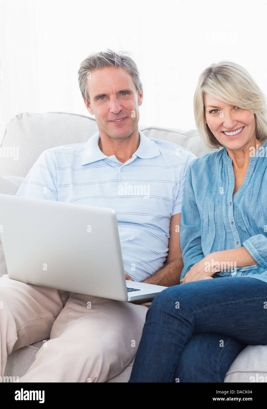 Couple using laptop together on the couch smiling at camera Stock Photo ...