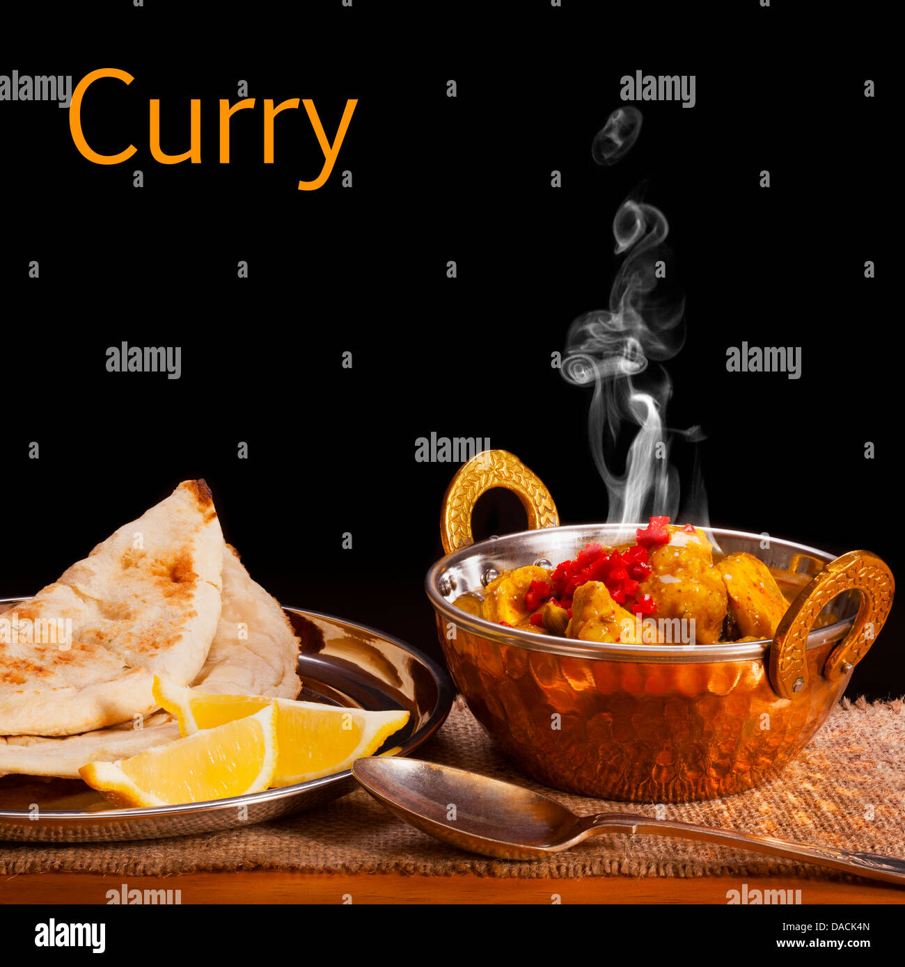 Curry Concept - a balti dish with chicken curry with visible steam rising, served with naan bread and lemon, front to back focus Stock Photo