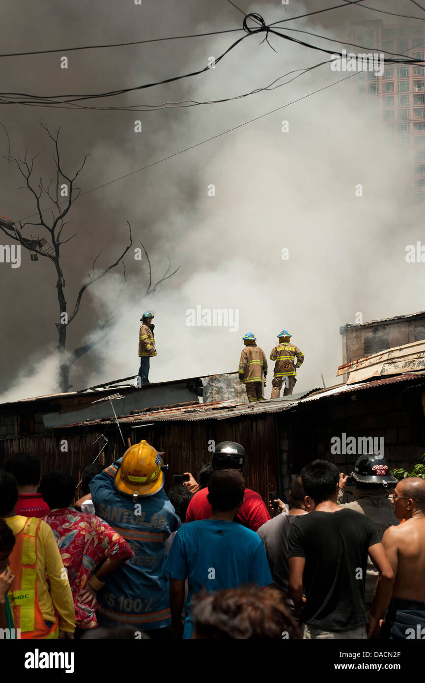 Crowd watch firemen hose down a fire in a shanty town in Makati City ...