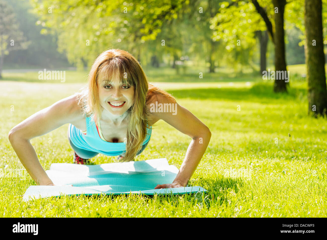 Female fitness instructor exercising doing pushups in green summer park Stock Photo