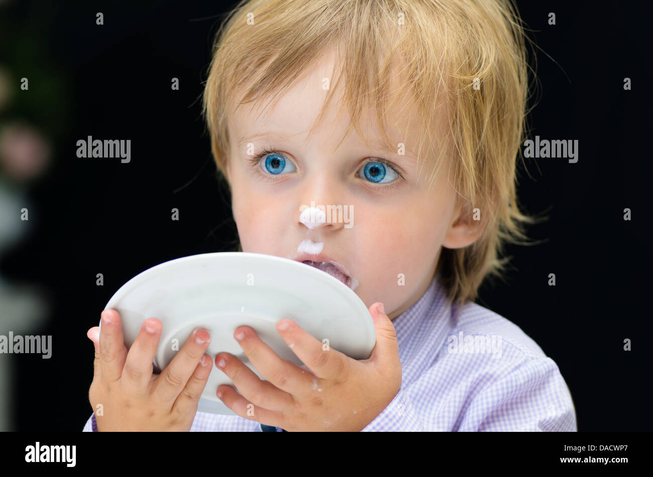 Little Boy Licking his Plate on black background Stock Photo
