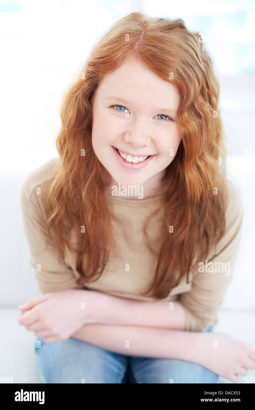 Vertical portrait of a cute red-haired girl sitting and looking at the camera Stock Photo