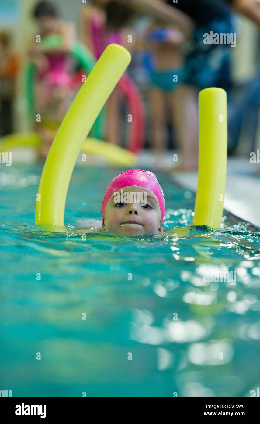 A fiveyearold girl swims in a pool with the help of a swimming noodle