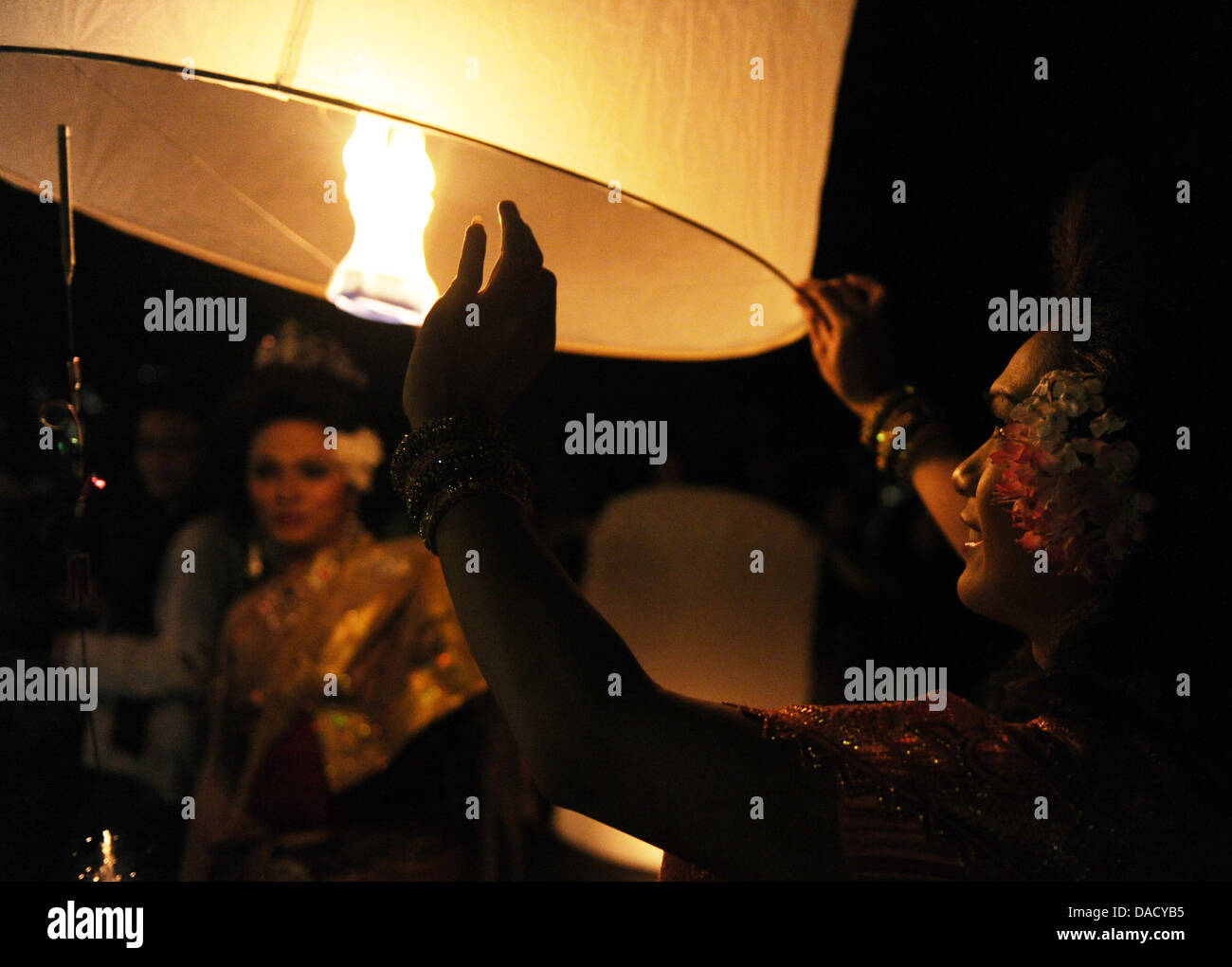 A woman dressed in a traditional Thai costume lights a paper lantern called Khom Loi at the Ping river during the festival of lights Loy Krathong in Chiang Mai, Thailand, 10 November 2011. The festival is celebrated in the whole country during full moon of the twelfth month of the year and originates from a Hindu tradition. Photo: Jens Kalaene Stock Photo