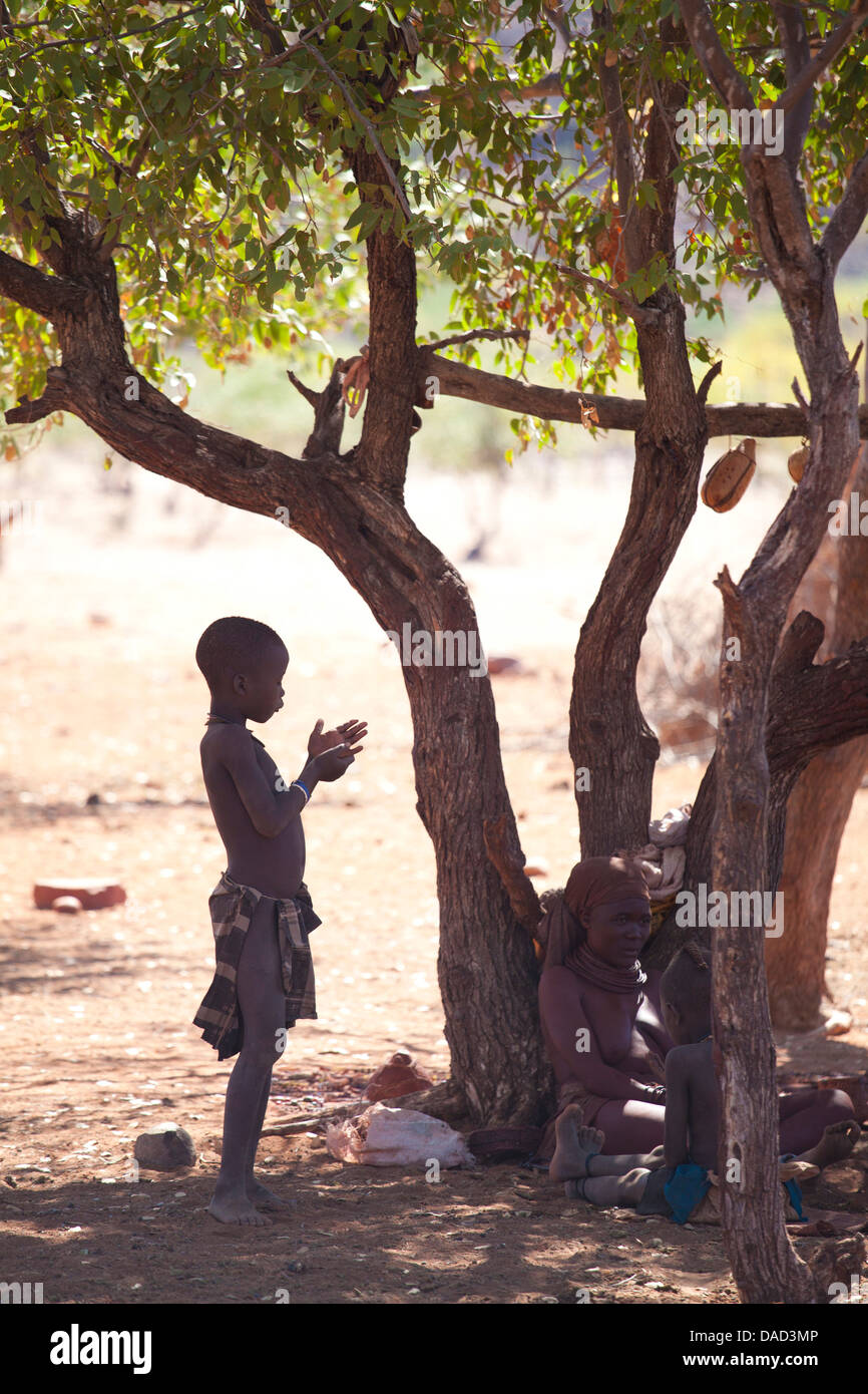 Himba boy standing in the shade of a tree in semi-silhouette, Kunene Region (formerly Kaokoland) in the far north of Namibia Stock Photo