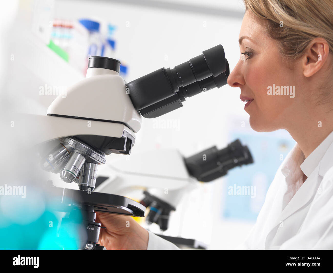 Female microbiologist viewing specimen under microscope in lab Stock