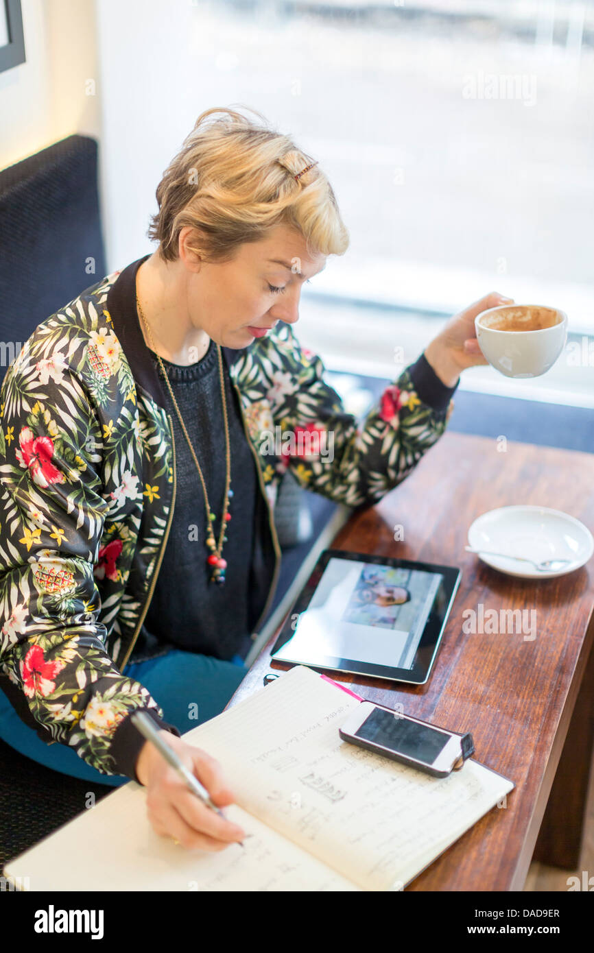 Woman making video call writing in notepad in cafe Stock Photo