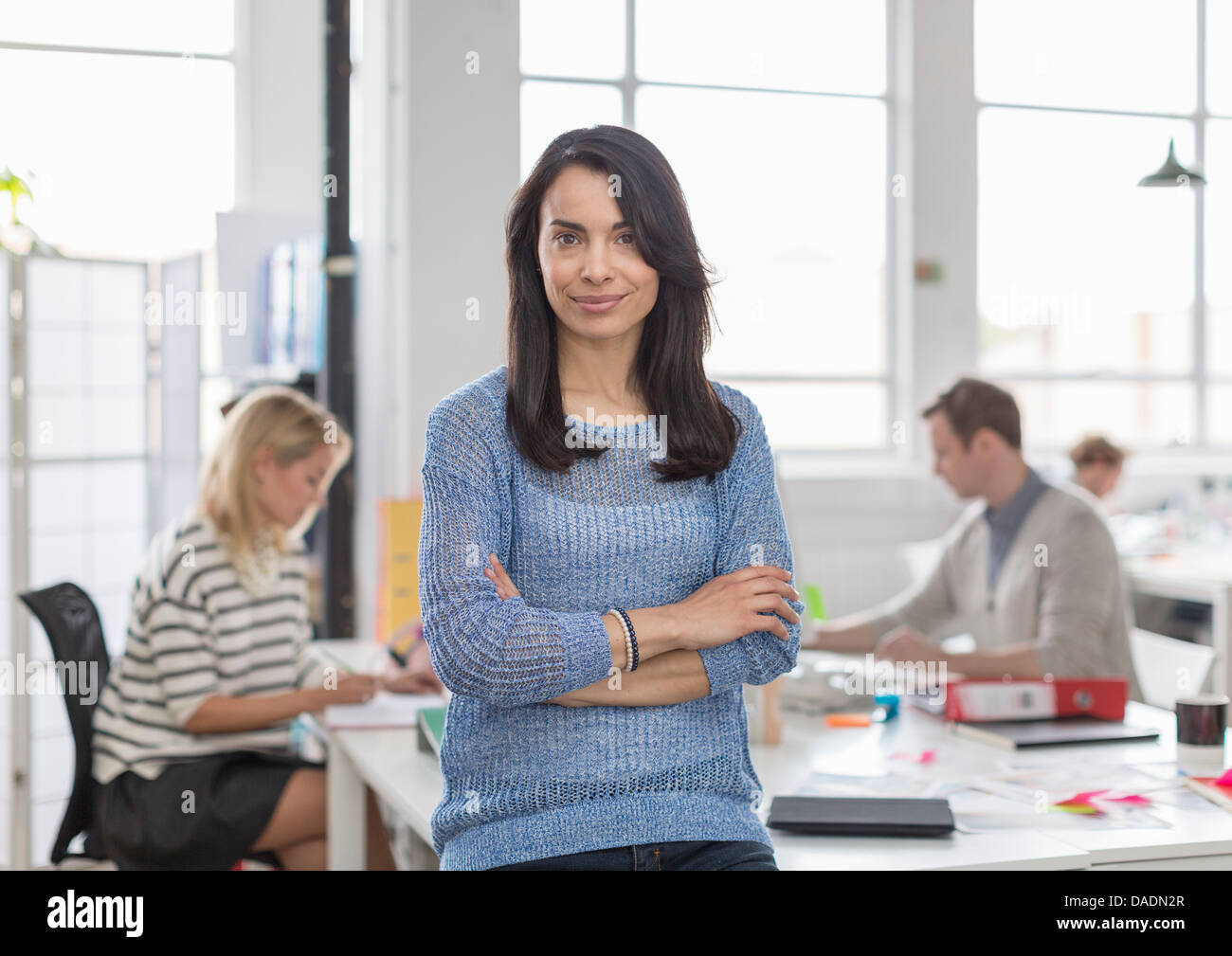 Mid adult woman sitting on desk and smiling in creative office, portrait Stock Photo
