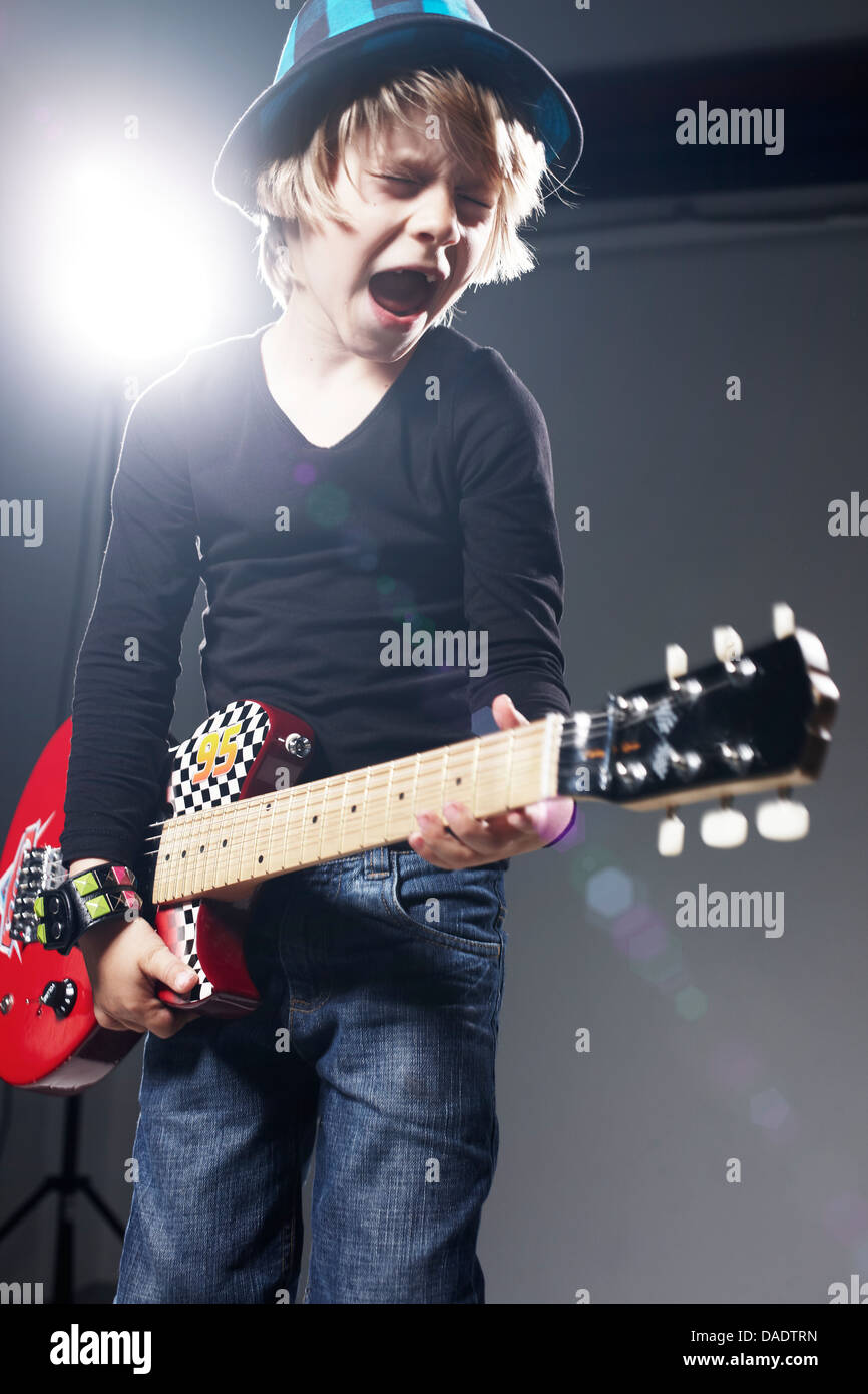 Boy playing paper guitar and singing against grey background Stock Photo